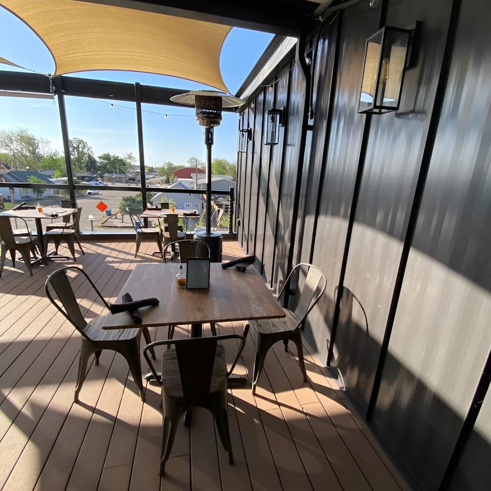 Sunny outdoor patio at Max & Louie's with tables, chairs, and a view of the surrounding area.