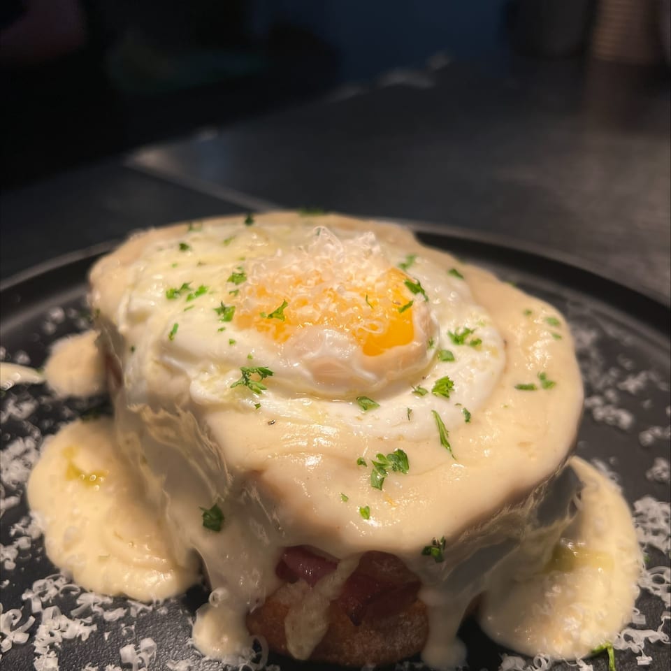 Max & Louie's breakfast dish with a fried egg, creamy sauce, and parsley on a dark plate.