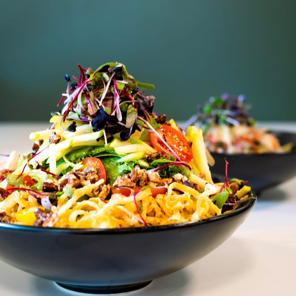 Two bowls of breakfast salad with greens, tomatoes, nuts, and crispy onions.