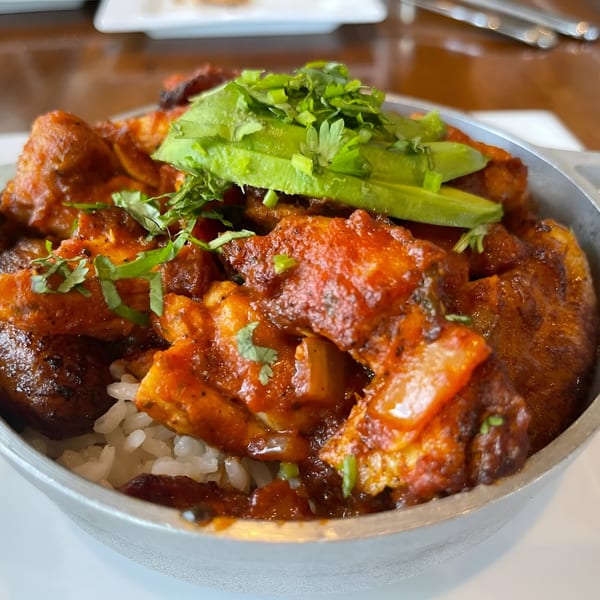 A close-up of a breakfast bowl with rice, saucy chicken, sliced avocado, and cilantro.