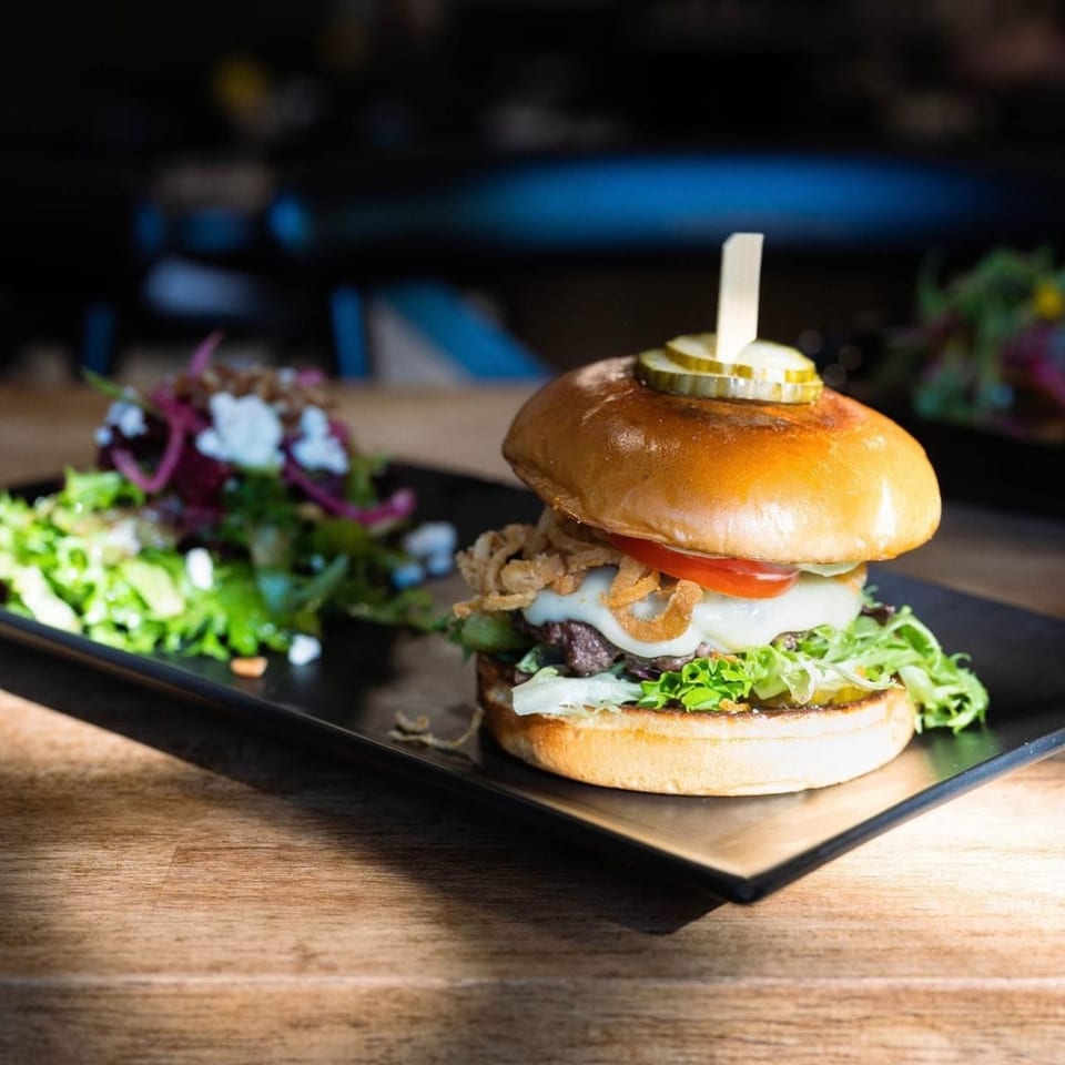 A Max & Louie's burger with melted cheese, crispy onions, and a side salad on a black plate.