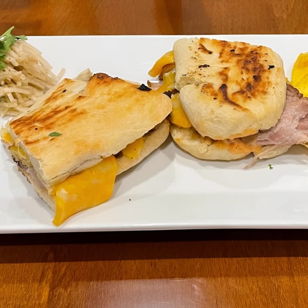 Two breakfast sandwiches with melted cheese and ham, served with hash browns on a white plate.